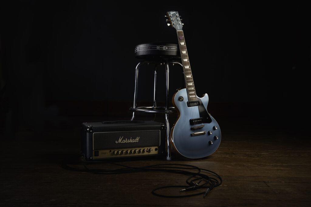 guitar leaning against a stool and fender amp. light painted professional photograph.