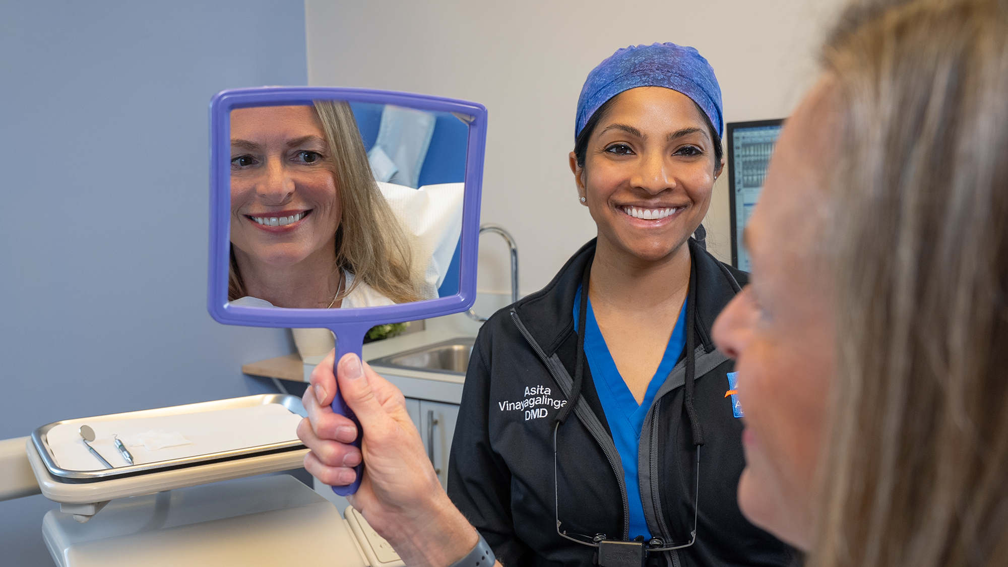 A dentist smiling with a patient holding a mirror, showing her reflection after treatment. Professional commercial photography capturing authentic healthcare services in Dayton, Ohio.