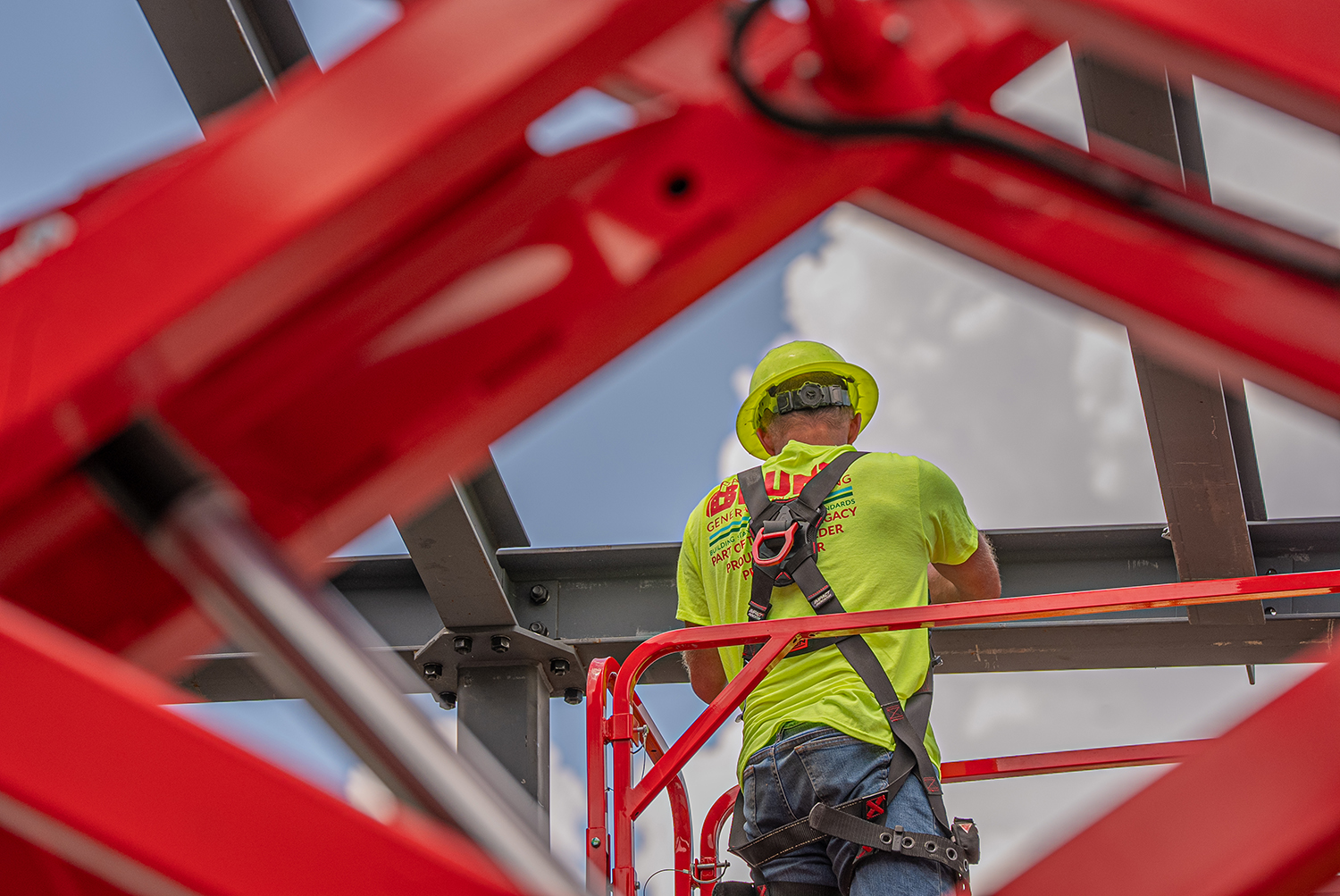Construction worker in safety gear on a red lift installing steel beams at a building site. Industrial and commercial photography showcasing construction services in Tipp City, Ohio.